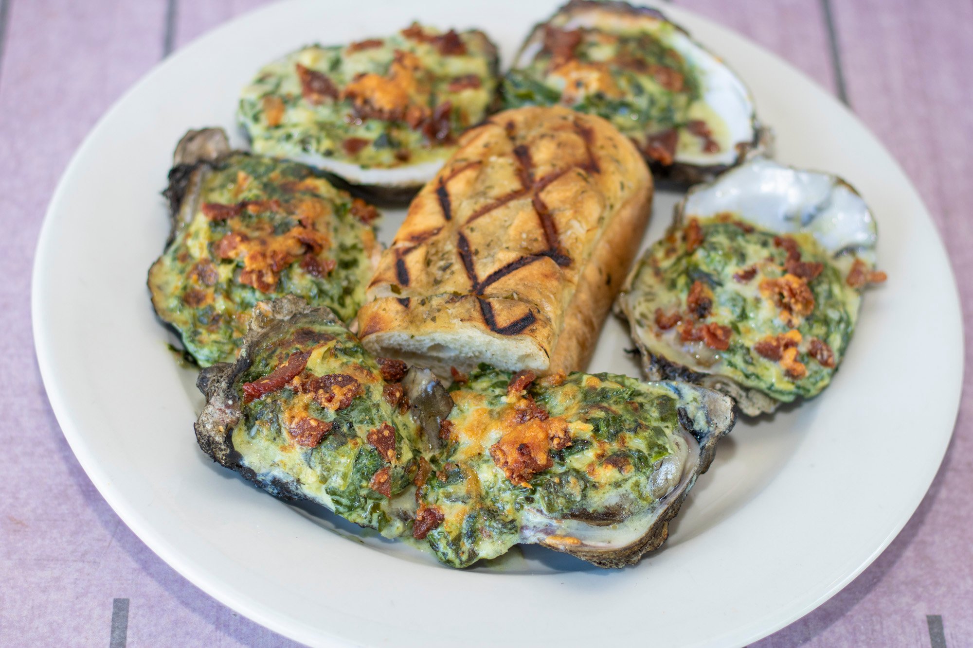 Half dozen freshly shucked oysters chargrilled with garlic butter and topped with spinach, artichokes, bacon, and parmesan cheese. Served with grilled bread.