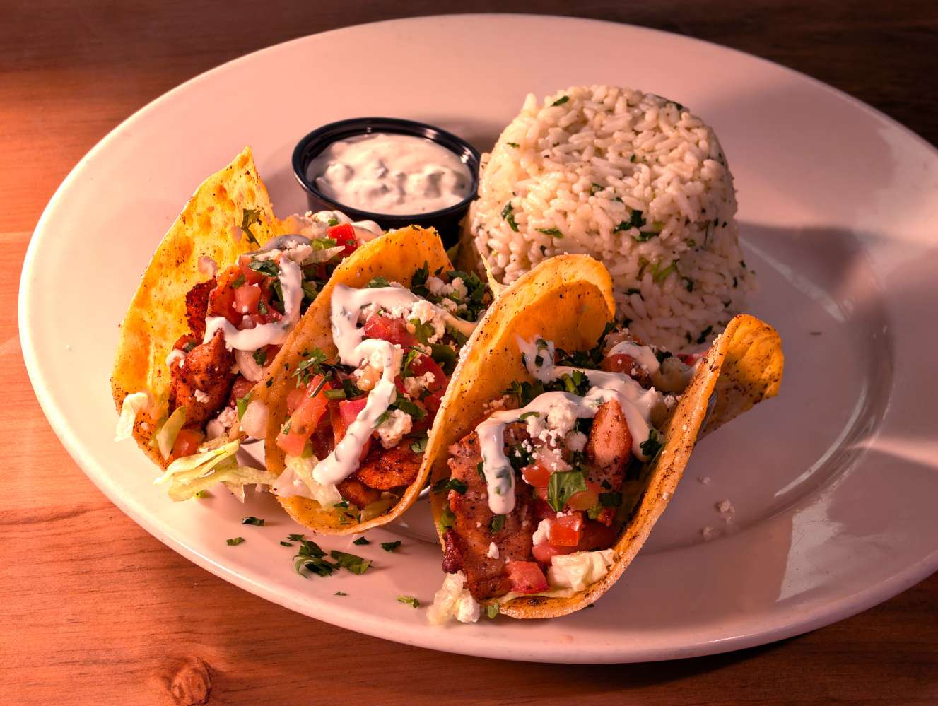 Three blackened salmon tacos with lettuce, cilantro lime crema, feta, and pico in toasted corn tortillas with cilantro lime rice