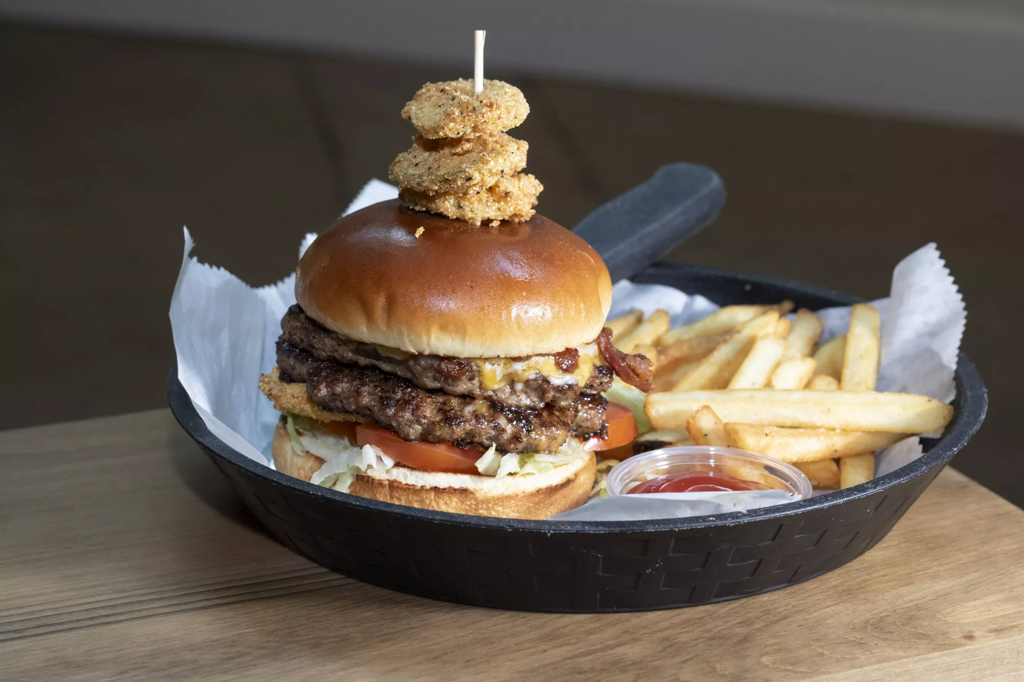 Two 4 oz beef patties topped with melty cheese, crumbled bacon, fried pickles, lettuce, and tomatoes, served with crispy fries