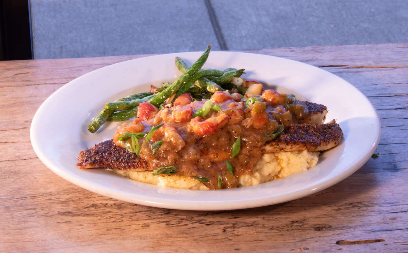 Pan-seared redfish in our signature blackening seasoning smothered in our from scratch crawfish étouffée on a bed of jalapeno cheese grits with a side of rockin' green beans